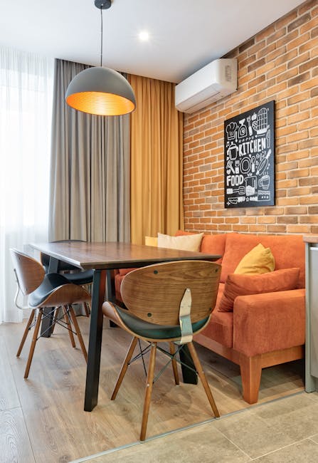 Contemporary interior with wooden table, chairs, and orange couch against a brick wall.